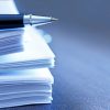 A ballpoint pen rests on top of a stack of documents ready for signing.  The image is photographed using a very shallow depth of field with the focus being on the tip of the pen.